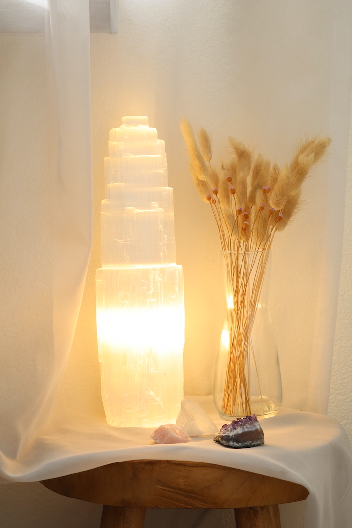 Grote Seleniet lamp van circa 35 cm hoog met warme witte gloed, naast glazen vaas met droogbloemen en edelstenen op houten tafel.