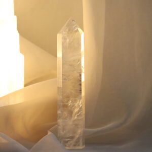 Heldere Bergkristal toren van 15 x 3 cm en 195 gram, staand in zacht warm licht met een serene, minimalistische achtergrond.