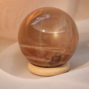 Bol van AA-kwaliteit Perzik Maansteen met Zonnesteen (4,2 cm) op een lichte houten standaard, sfeervol gefotografeerd in warm, zacht diffuus licht.