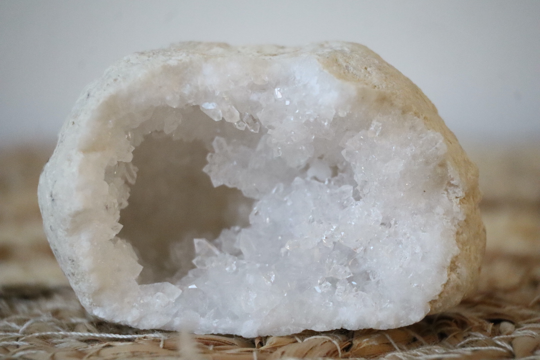 Marokkaanse Bergkristal Geode van 134 gram met fonkelende witte kristallen en een matte buitenkant, gefotografeerd op een natuurlijke ondergrond.