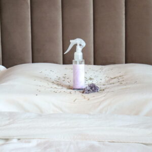 Zijdezachte Nachtrust pillow spray van Spiritueel Wonen, lavendel-kamille-ylang-ylang, geplaatst op een zacht bed met amethistkristal en lavendelbloemetjes.