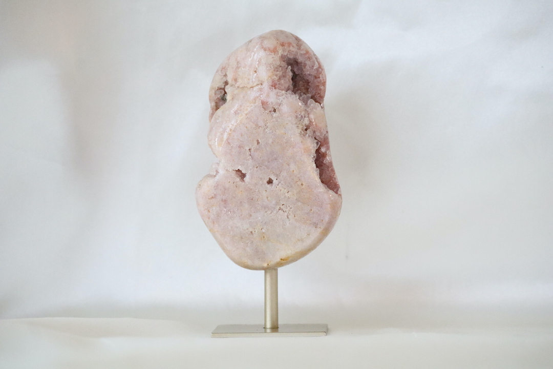 Druzy roze chalcedoon op goudkleurige metalen standaard met zachte poederroze tinten en open kristalstructuren, gefotografeerd in natuurlijk daglicht.