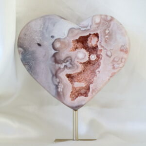 Druzy chalcedoon hart op metalen standaard met zachte beige en crème tinten en een open kristalholte, gefotografeerd in natuurlijk daglicht.