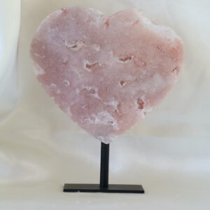 Druzy roze chalcedoon hart met kwarts op zwarte metalen standaard, gepolijste hartvorm met zachte poederroze tinten en subtiele kristalstructuren, gefotografeerd in natuurlijk daglicht.
