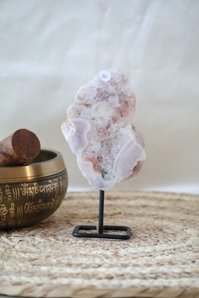 Roze chalcedoon met kwarts op zwarte metalen standaard, zachte roze en witte kristalstructuren, gefotografeerd in natuurlijk licht op een rustige interieurachtergrond.