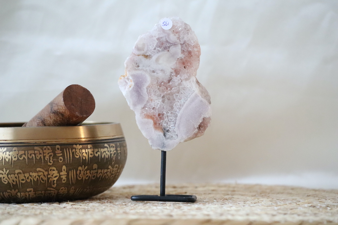 Roze chalcedoon met kwarts op zwarte metalen standaard, zachte roze en witte kristalstructuren, gefotografeerd in natuurlijk licht op een rustige interieurachtergrond.