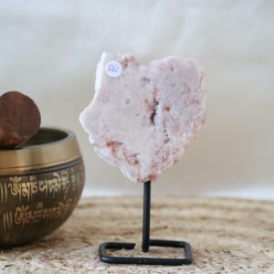 Roze chalcedoon op zwarte metalen standaard, zachte poederroze tinten en licht kristallijne structuur, gefotografeerd in natuurlijk daglicht op een rustige interieurachtergrond.