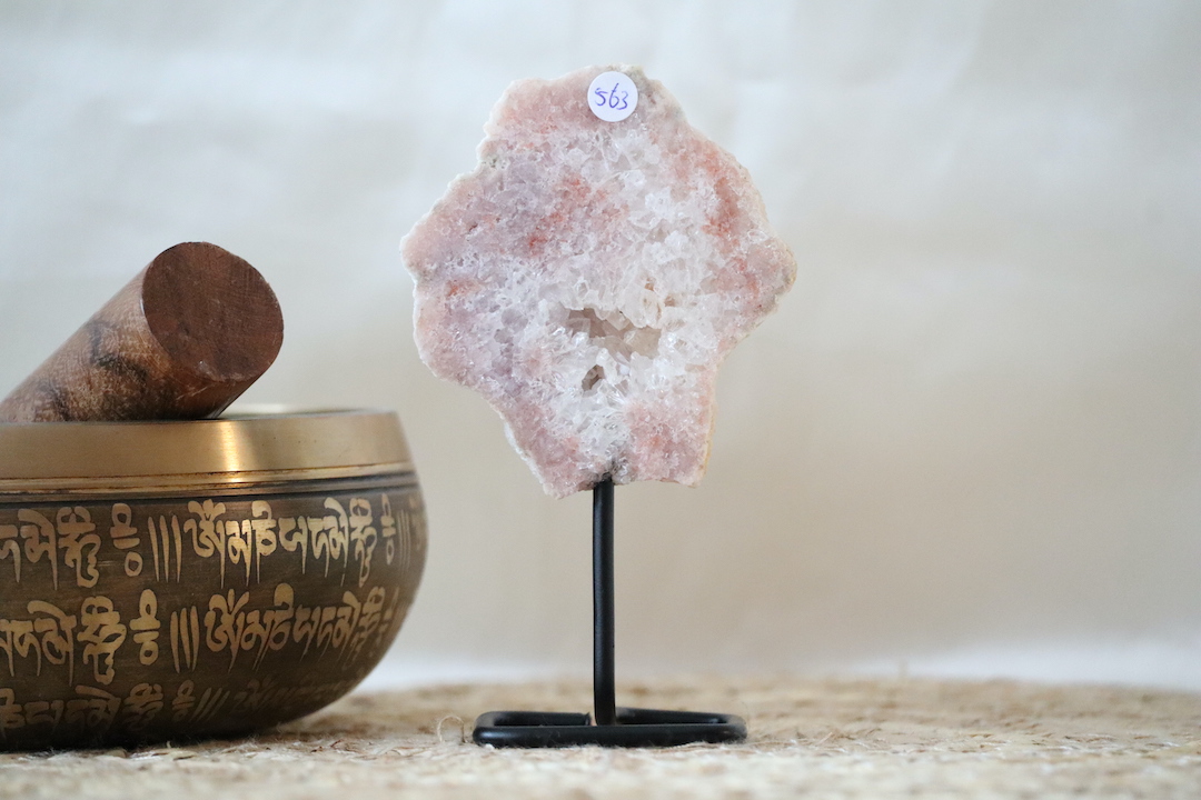 Roze chalcedoon met kwarts op zwarte metalen standaard, zachte poederroze tinten en heldere kristalstructuren, gefotografeerd in natuurlijk daglicht tegen een rustige interieurachtergrond.