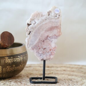 Roze chalcedoon op zwarte metalen standaard met zachte roze bandstructuren en licht kristallijne delen, gefotografeerd in natuurlijk daglicht op een rustige interieurachtergrond.