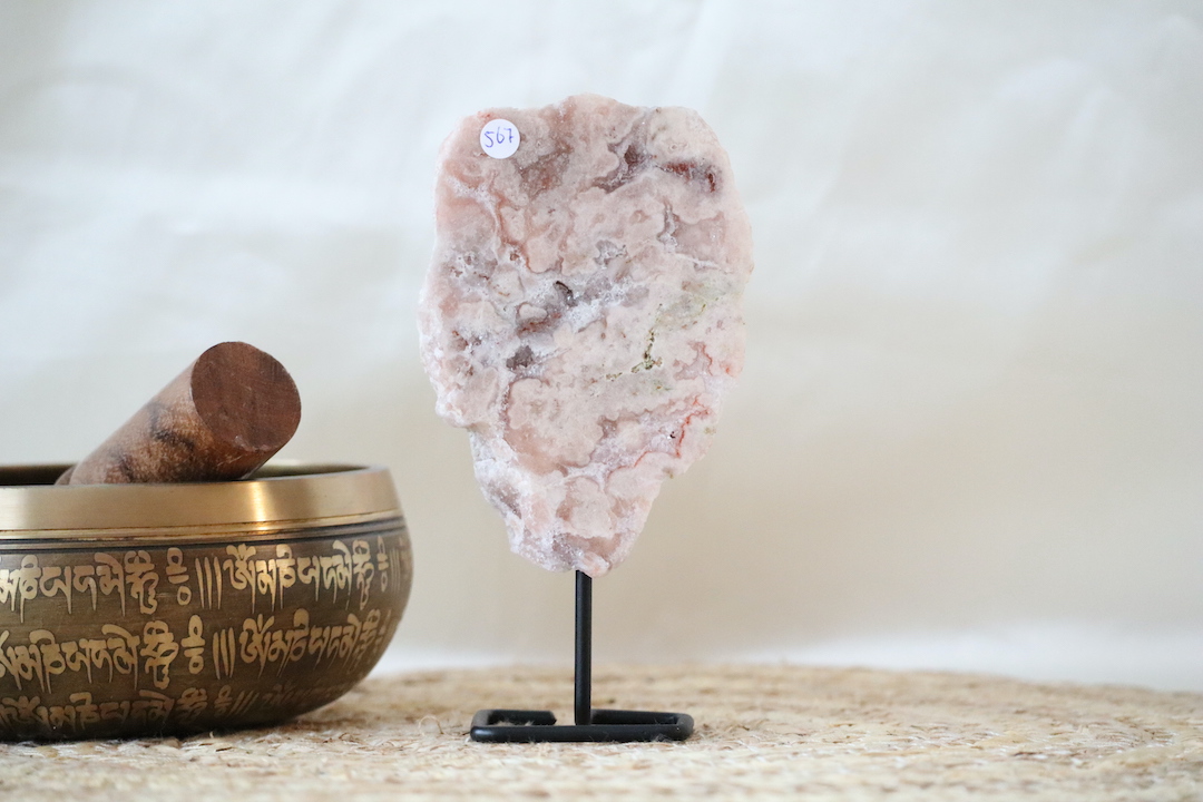 Roze chalcedoon met kwarts op zwarte metalen standaard, zachte poederroze tinten met natuurlijke adering en lichte kristallijne structuren, gefotografeerd in natuurlijk daglicht.