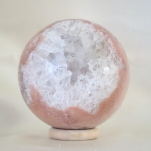 Roze chalcedoon met kwarts bol met perzikroze tinten en helder kwarts met subtiele regenboogreflecties, gefotografeerd in zacht natuurlijk licht.