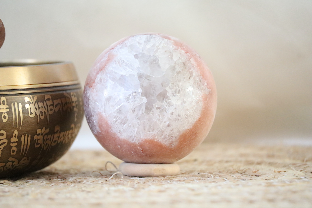 Roze chalcedoon met kwarts bol met perzikroze tinten en helder kwarts met subtiele regenboogreflecties, gefotografeerd in zacht natuurlijk licht.