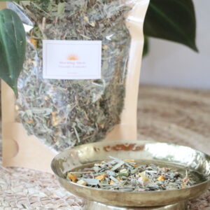 Close-up van Morning Glow kruidenthee in een messing schaaltje met zichtbare citroengras, sinaasappelschil en gemberstukjes.