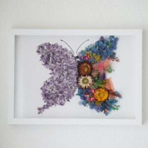 Handgemaakte vlinder wanddecoratie met amethist kristallen en gedroogde bloemen in witte lijst.