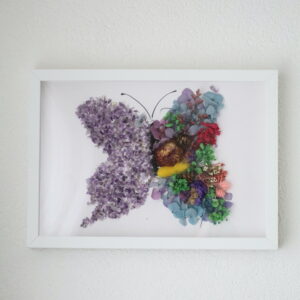 Handgemaakte vlinder wanddecoratie met amethist kristallen en gedroogde bloemen in witte lijst.