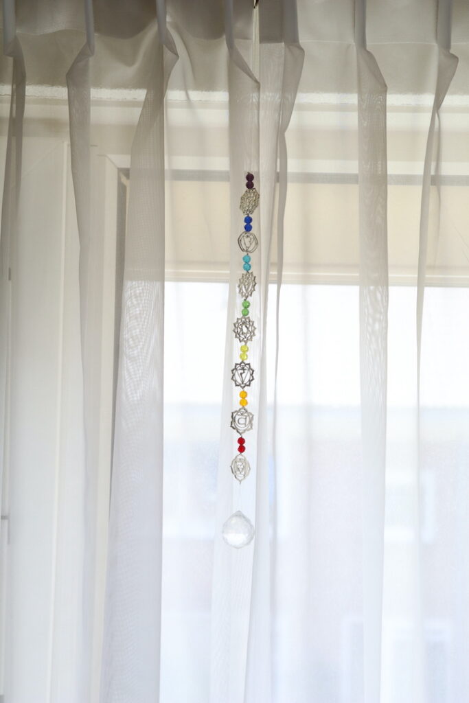 Chakra zonnevanger van 46 cm hangend voor een raam met zeven chakrasymbolen en kristalhanger.