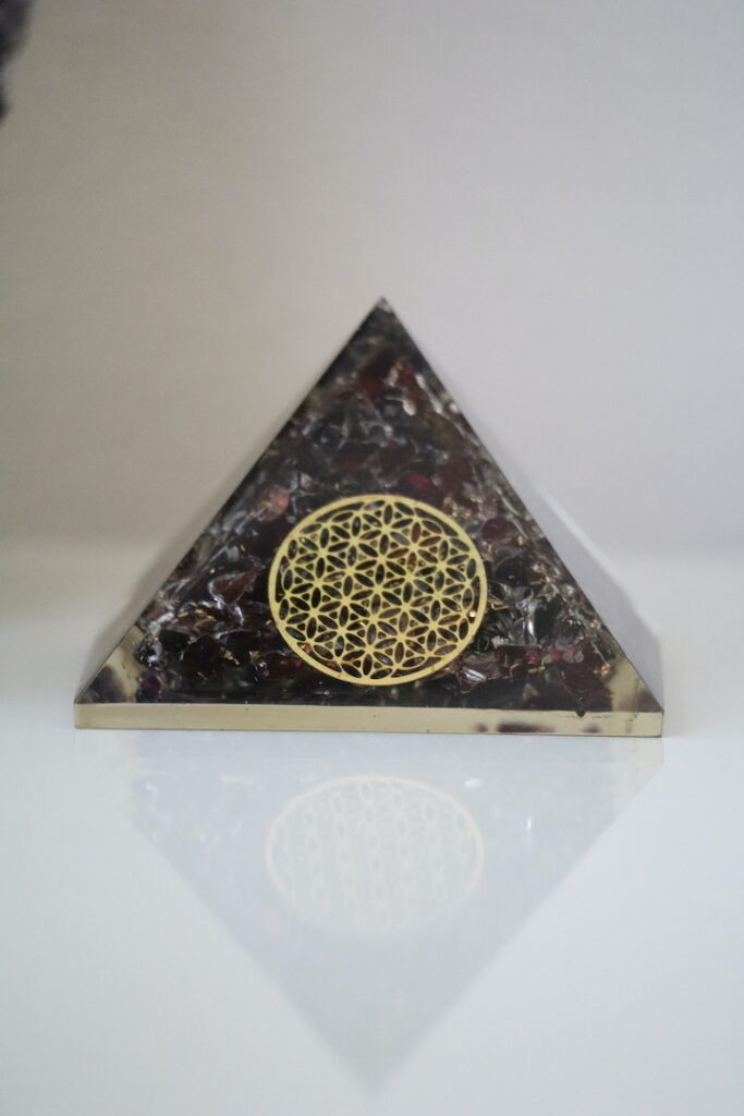 Granaat Orgoniet Piramide met Flower of Life op een witte achtergrond.