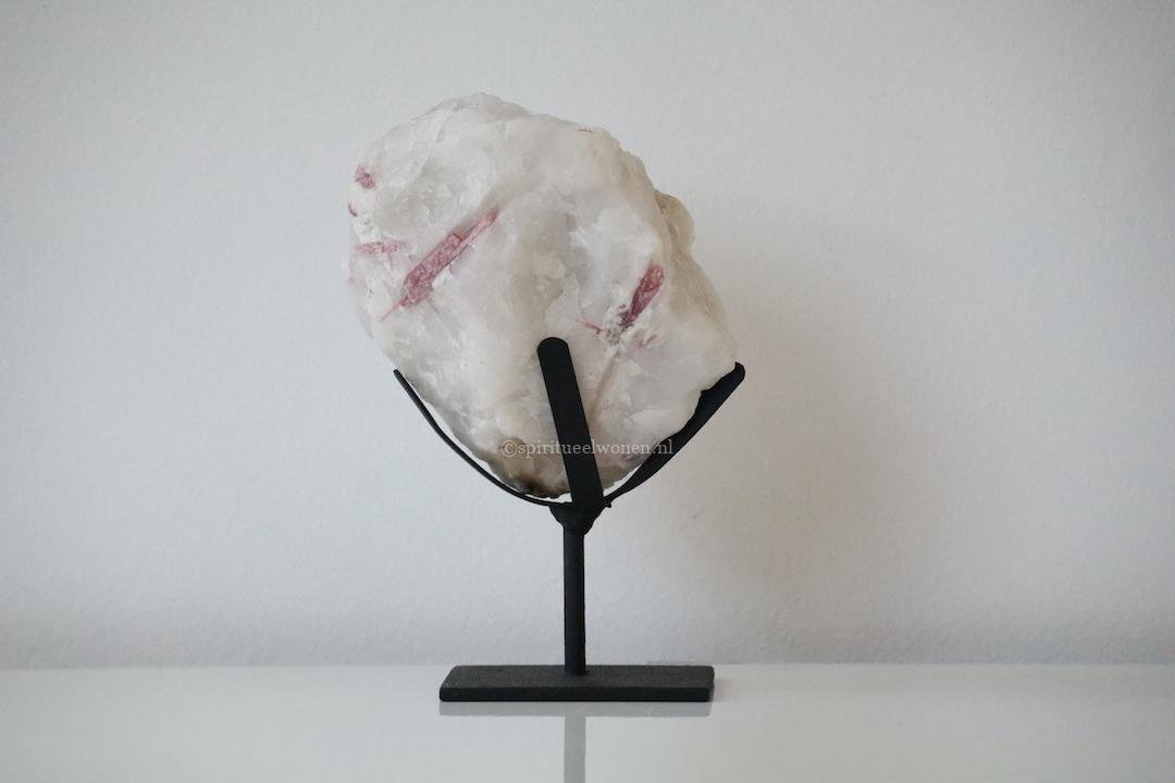 Roze toermalijn in kwarts op zwarte standaard als natuurlijke decoratie in een licht interieur.