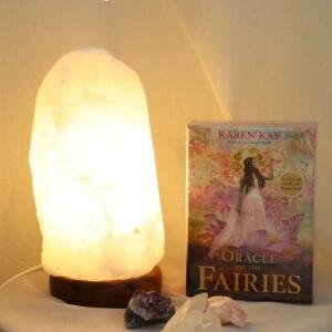 Witte zoutlamp 1-2 kg met warme verlichting naast Oracle of the Fairies orakelkaarten en edelstenen.