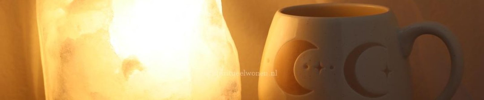 Witte zoutlamp met warme verlichting naast maanfasen mok, amethist, bergkristal en rozenkwarts.